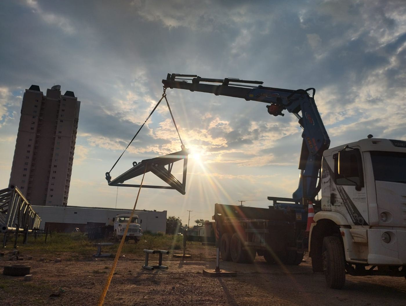 Caminhão Munck da LF içando treliça ao pôr do sol
